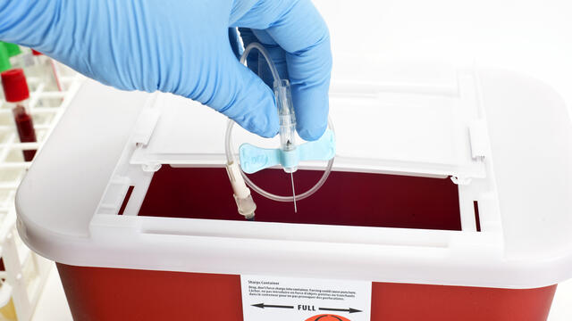 Gloved hand dropping catheter into sharps disposal box