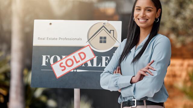 Person standing next to a For Sale sign with a sold sticker