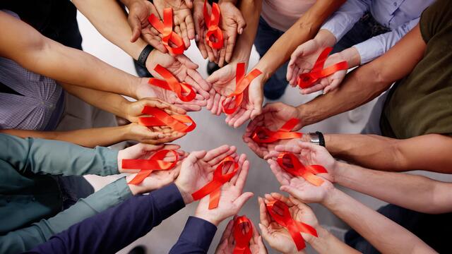 Aerial view of a circle of hands holding HIV-AIDS red ribbons