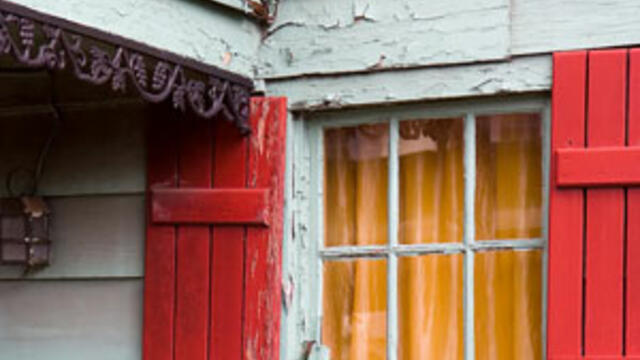 White house with red shutters showing peeling and flaking lead paint.