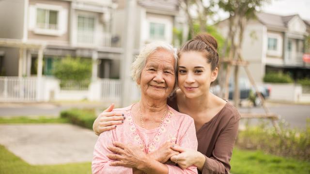 An adult being hugged by a caregiver front of a house.