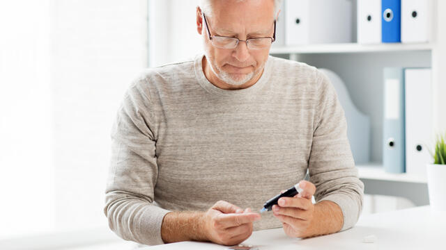 An adult uses a glucometer on a finger.