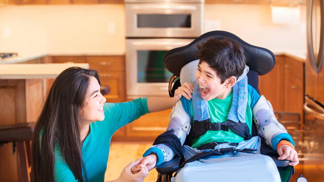 adult laughing with a child in a wheelchair in a kitchen