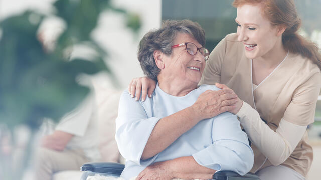 Happy patient in a wheelchair and caregiver clasping hands
