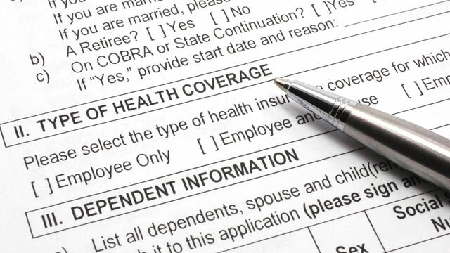 Close up of an insurance form, type of health coverage and dependent information, with a pen resting on the paper