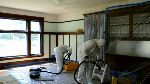 Two adults in full hazmat suits doing renovation in a room.