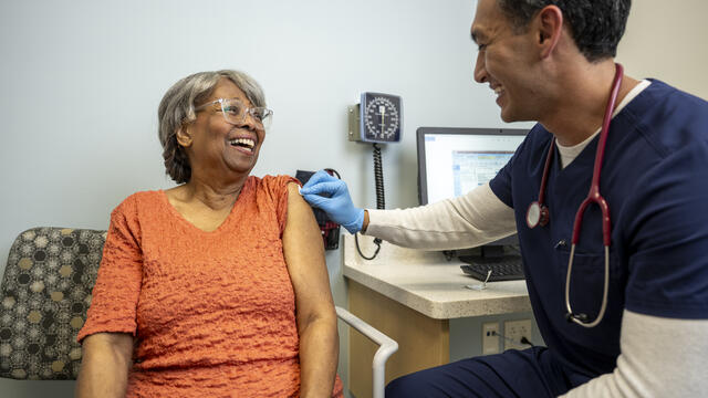 An adult gets a vaccine by a nurse in a clinic setting