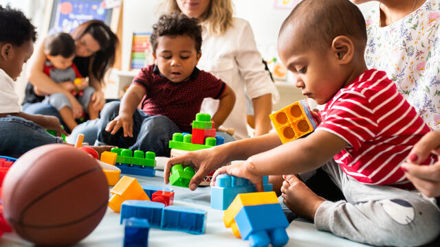 Toddlers sitting on adult laps playing with building blocks