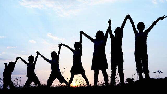 A silhouette of children standing and holding hands in the sky