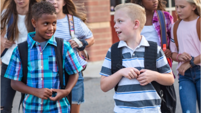 Several kids wearing backpacks and walking