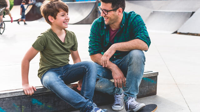 Adult and child with a skateboard, sitting and talking at a skateboard park