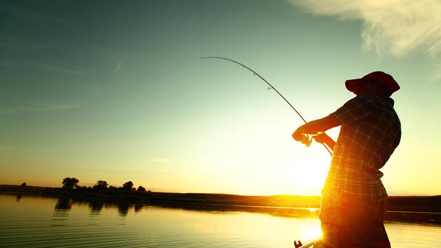 An adult reels in a fish at sunset on a boat