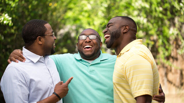 Three adults hug and laugh in a park