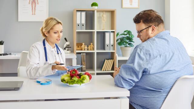 A nutritionist with a bowl of vegetables on their dest discusses diet with a patient