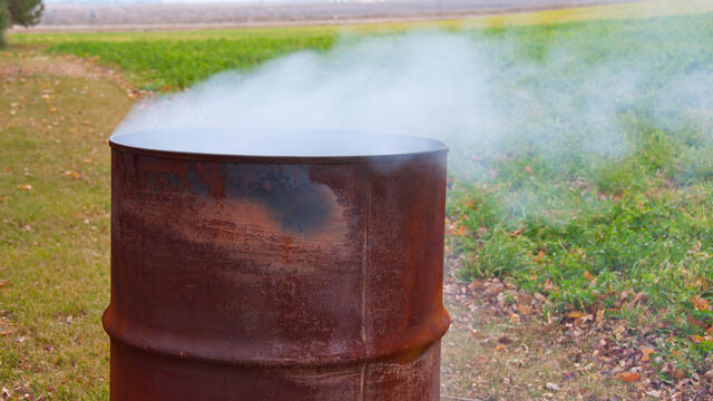 Rusted mental trash can in an open field with smoke coming out of it