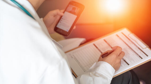 Medical professional checking smart phone and updating chart