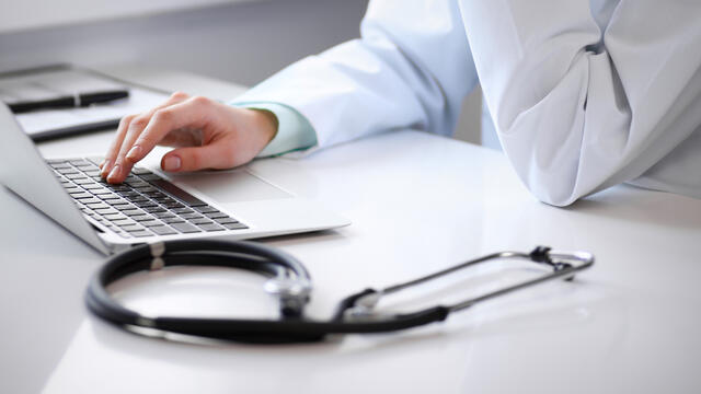 Doctor's hand on a laptop next to a stethoscope