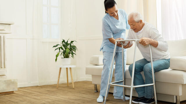 Caregiver assists an adult to use a walker to rise from a sofa