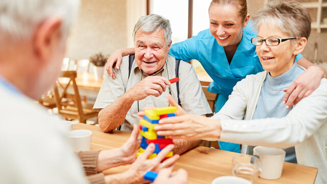 Older adults with a caregiver building with legos at a table.