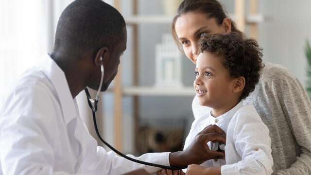 Child sitting on adult's lap while doctor listens to their heart