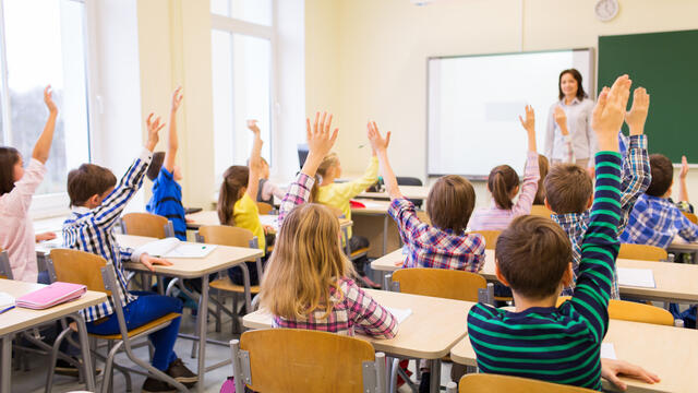 Students in a classroom raising their hands to answer a question