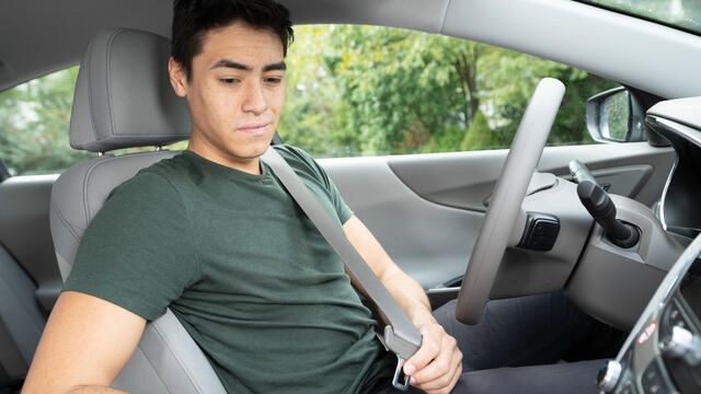 A teen sits in a car buckling their seatbelt.