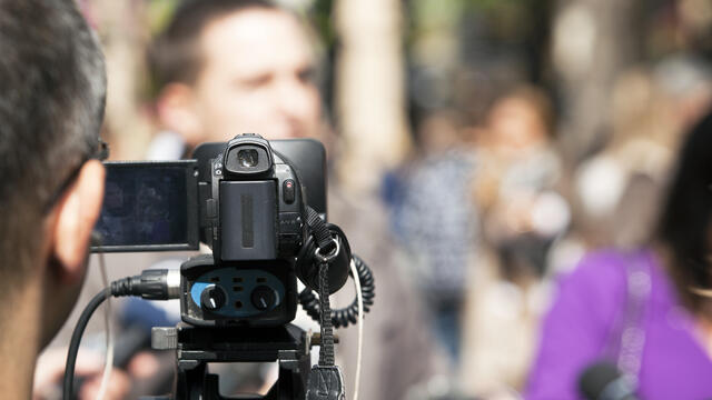 A video camera records blurred audience.