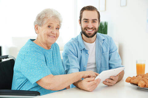 Caregiver holding a tablet sitting with an older adult at a table