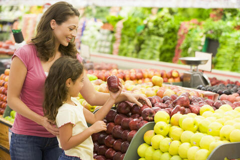 An adult and a young child shopping in the produce section, looking at apples
