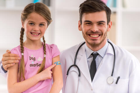 A doctor and smiling child with a bandaid on arm after receiving a vaccine