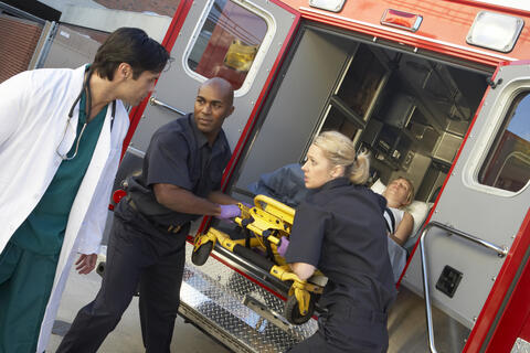 Photograph of two EMTs and a doctor unloading a patient from an ambulance.