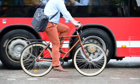 An adult with a briefcase rides bicycle next to a bus.