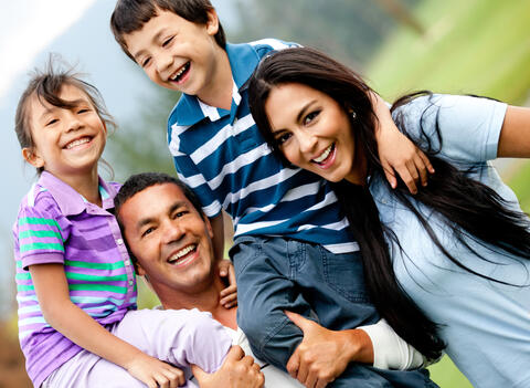 A happy family of four with two kids on their shoulders.