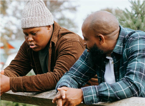 Two people talk while leaning on a railing