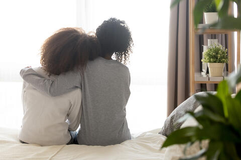 Adult with arm around teen sitting on a bed