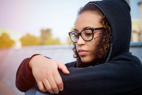 A sad teen sitting with arms around knees near the water