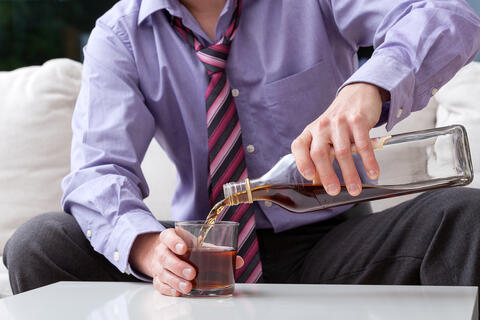 adult pours alcohol from a bottle into a glass