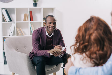 A seated adult talking to an adult with their arm around a child