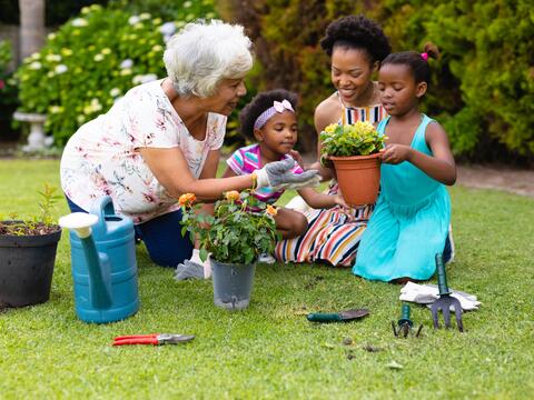 Older adult shows an adult and two children how to pot flowers