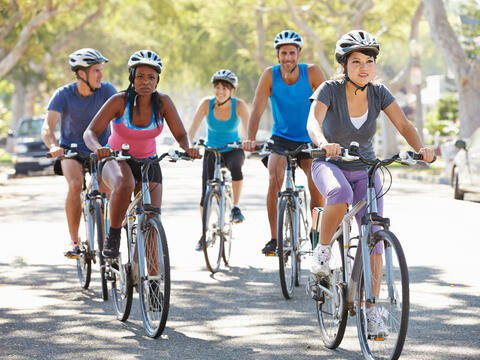 Five adults with helmets riding their bicycles down the street.