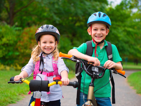 Two smiling children with their bicycles on a bike path.