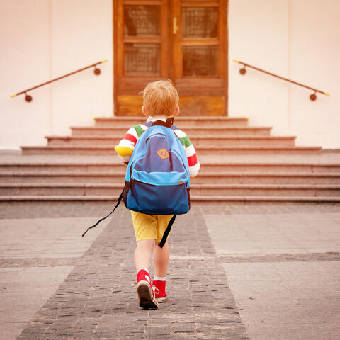 A child with a backpack walking toward school steps