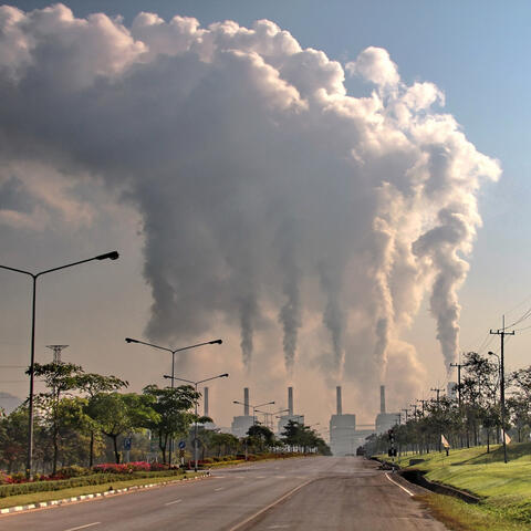 A road leading to seven smokestacks in the distance giving off smoke
