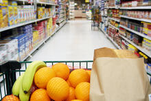Shopping cart in grocery aisle with oranges, bananas and a brown paper bag