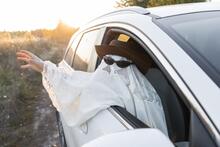 Child dressed as a ghost with hat and sunglasses sits in car with arm out open window