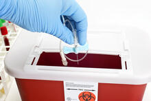 Gloved hand dropping catheter into sharps disposal box