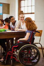 A smiling teacher works with a child sitting in a wheelchair