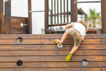 Young child climbing over a playground climbing wall.