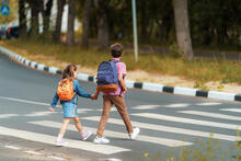 Two children wearing backpacks use a crosswalk to cross the street