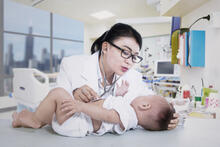 Baby on exam table while doctor listens to their heart using a stethoscope